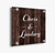 "Clear acrylic sign featuring 'Chris & Lindsey' in elegant white script, displayed on a rustic dark woodgrain background with metal standoffs for a modern, personalized touch."