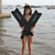 Woman in water holding black Los Niños Freedive Fins with coastal harbor background