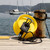 Ocean Guardian Shark Shield for Swimming in yellow protective casing, displayed on wooden dock with sailboats and coastline in background