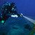 Diver holding 1700 Lumens Dive Light underwater, illuminating blue ocean depths with bright beam against rocky seafloor