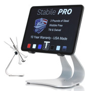 Stabile PRO silver steel iPad stand holding an iPad in landscape orientation, screen displaying features: 3 pounds of steel, wobble free, tilt and swivel, USA made 10 year warranty. Small inset shows tilt motion range on left.