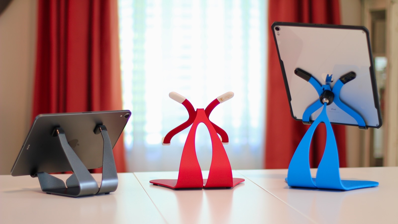 3 iPad stands on a desk, space gray, red and blue colors