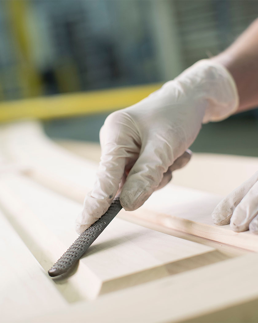 Gloved hand of a Masterpiece artisan sanding a cabinet door using a tool