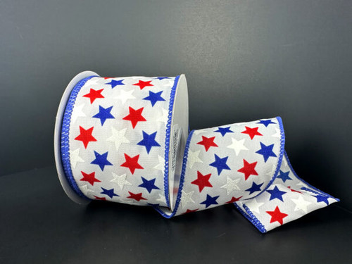A 2.5 inch wide roll of white satin wired ribbon with a scattered pattern of solid red, blue, and white stars and a blue stitched edge.