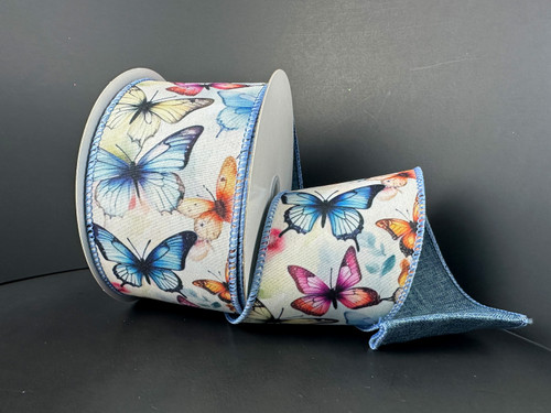 A 2.5 inch wide roll of light-colored poly linen wired ribbon featuring a dense pattern of vibrant blue, orange, and pink butterflies with a blue stitched edge.