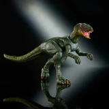 Mattel Hypsilophodon Jurassic World Hammond Collection 8-Inch Action Figure, detailed green dinosaur toy with open mouth showing teeth, posed on a reflective black surface with a dark background and a spotlight shining on it.
