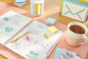 Post-it Notes 38x51mm 100 Sheets Canary Yellow (Pack 12), image showing a desk with various colorful sticky notes, a planner, a pen, a cup of tea, and organized stationery items.