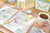 Post-it Recycled Z-Notes 76x76mm 100 Sheets Per Pad PEFC Canary Yellow, stack of colorful sticky notes on a desk, alongside a notebook, pen, cup of tea, and other office supplies.