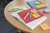 Post-it Post it Super Sticky Notes Boost Colours 76x127mm 90 Sheets Pack 5, colorful sticky notes placed on assorted notebooks and paper on a desk.