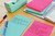 Post-it Super Sticky Notes 101x152mm Ruled 90 Sheets Cosmic Colours Pack 3, colorful sticky notes on a desk with writing and stationery.