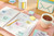 Post-it Notes 38x51mm 100 Sheets Canary Yellow (Pack 12), image showing a desk with various colorful sticky notes, a planner, a pen, a cup of tea, and organized stationery items.