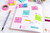 Post-it Note Cube 76x76mm 450 Sheets Pastel Pink 2028P - 7100172384, a cube of pastel pink sticky notes with 450 sheets placed on an open planner with colorful notes and stationery around.