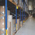 CW Office Durable Adhesive Aisle Sign A5 PK10, image of warehouse aisle with blue and yellow shelving racks containing boxes and pallets.