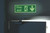 CW Office Niteglo Exit Man Arrow Down S/A 15X45, illuminated green fire exit sign with arrow pointing downward and running figure.