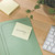 CW Office Post-It Yellow Z-Notes 76X76MM PK6, a yellow sticky note with handwritten text 'Wichtig!' placed on a green file folder on a wooden desk.