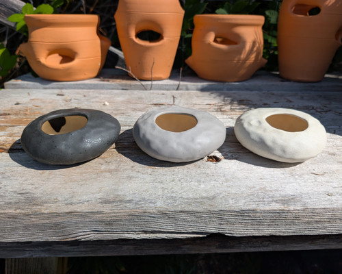 Smooth ceramic rock-shaped planters available in charcoal, light grey, and white.