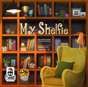 Board game box featuring game title and bookshelf with an orange cat a green arm chair Board game box featuring game title and bookshelf with an orange cat a green arm chair