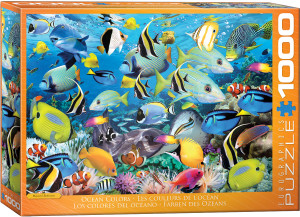 The image shows the box of a puzzle featuring a vibrant underwater scene with a variety of colorful tropical fish swimming among coral reefs. The background is a deep blue, representing the ocean. Fish in diverse colors such as yellow, blue, black, and white swim in various directions, showcasing species like angelfish, tangs, and clownfish. The coral is depicted in hues of purple, pink, and white, adding to the dynamic atmosphere.  The title, "Ocean Colors" is printed in white text on an orange background along the bottom edge. Along the right hand edge, the company logo reads "EUROGRAPHICS PUZZLES" and the number ‘1000’ after it indicates the puzzle piece count.