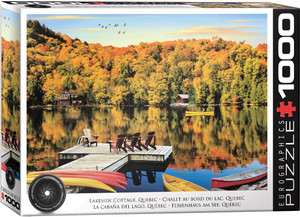 The image displays a serene lakeside scene in autumn. In the foreground, a wooden dock extends into a calm lake, with several Adirondack chairs and a few canoes and kayaks in vivid colors like yellow, red, and orange resting by the dock. The water reflects the vibrant autumn foliage of the forest on the opposite shore, showcasing trees in shades of yellow, orange, and red. Two small cottages are nestled among the trees. Above the lake, a clear blue sky is visible with a flock of birds flying in formation. The title, "Lakeside Cottage, Quebec" is printed along the bottom edge. On the right hand edge, the company logo reads "EUROGRAPHICS PUZZLES" in white text on black background and the number ‘1000’ after it indicates the puzzle piece count. In the bottom left, there is a picture of a camera lens with the words "HDR Photography - Scenic Landscape" printed on the inside rim of the lens.