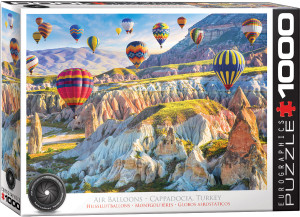 A puzzle titled, “Air Balloons over Cappadocia, Turkey,” at the bottom in several different languages.  The company logo “Eurographics Puzzle” is in large font along the right side, and number ‘1000’ right next to it in the cover’s black and white border.  In the center is what the completed puzzle looks like: an aerial view of air balloons floating above green plateaus and mountains.  The balloons feature bright colors and patterns that distinguish them from both the surrounding landscape and each other, likely for both spotting from a distance and search and rescue purposes.