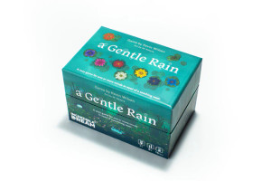 A board game titled "A Gentle Rain" across the front and top of a small box in white font that takes up most of the space.  Below the title are eight different colored lilies floating atop a backdrop of a teal lake that has gentle water droplets rippling across the surface. A board game titled "A Gentle Rain" across the front and top of a small box in white font that takes up most of the space.  Below the title are eight different colored lilies floating atop a backdrop of a teal lake that has gentle water droplets rippling across the surface.
