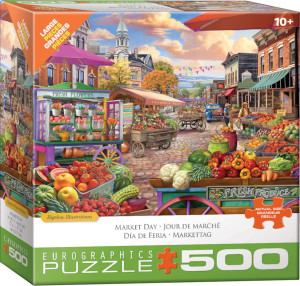 A puzzle titled, “Market Day,” at the bottom in several different languages, with the artist's name right above it.  The company logo “Eurographics Puzzle” is in large font along the bottom, and number ‘500’ right next to it in the cover’s green border.  In the center is what the completed puzzle looks like: a cobblestone-paved town square with wooden trolleys and stalls filled with fruits, vegetables, and flowers.  People mill about the stands between brick buildings under a blue sky.