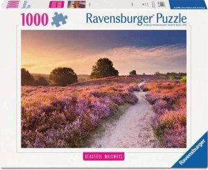 A puzzle with the words “Ravensburger Puzzle” at the top and the number ‘1000’ along the left side of the white bordered cover.  Below is an image of the finished puzzle, which features a photograph of a sandy path cutting through fields of wild thyme and heather, both of which are pink atop their bushes.  The sun sets orange and pink in the sky.
