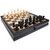 A chess set with dark stained wood for the outer board, half of the squares in the grid, and the chess pieces in the foreground and light wood for the other half of the squares and pieces.  The black board is thick to accommodate a drawer in the middle with a little knob handle.