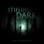 A board game titled "The Stifling Dark", the tall, green letters of which are partially shrouded by the dark board art.  Most of the cover is pitch black, with a small area illuminated in the center depicting a small silhouette in a forest holding a flashlight that reveals the trunks of tall trees that surround them.  The dark is, indeed, stifling.