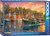 The image shows the box of a puzzle featuring the piece “Harbor Sunset” by Dominic Davison. The artwork depicts a vibrant harbor scene at sunset. Several fishing boats are anchored at the dock, with the prominent green boat in the foreground named "Cormoran." The water reflects the warm colors of the sunset sky, a blend of pink, orange, and purple hues. On the left, a quaint village with Victorian-style houses, painted in shades of blue and brick red, lines the waterfront. Trees with lush green foliage stand behind the buildings. A few birds, including a seagull, fly across the sky, while one seagull is perched on a wooden post in the foreground. Along the right hand edge  the company logo reads "EUROGRAPHICS PUZZLES" in white text on a blue background. The number ‘1000’ printed after it indicates the puzzle piece count. Along the bottom edge the title is printed in several different languages.