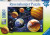 A puzzle with the words “Ravensburger Puzzle” at the top and the number ‘500’ along the left side of the white and green-bordered cover.  Below is an image of the finished puzzle, which features 6 of the planets in our solar system posed far too close together for gravity to allow them not to smash into one another.  Behind them are distant stars, galaxies, and nebulae.