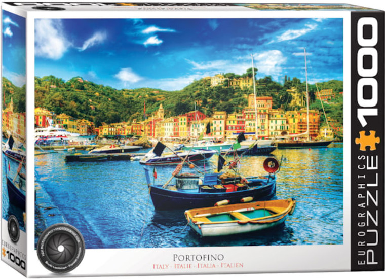 A puzzle titled "Portofino Italy" at the bottom with large, white font within a black text box along the side that has the number "1000" in it.  In the center is a photograph of a town at the feet of short mountains that are covered in brush and trees.  The town is made up of yellow plaster and terracotta roofing, and in front of it is a small port with clear blue water and boats of all shapes and sizes tied up.