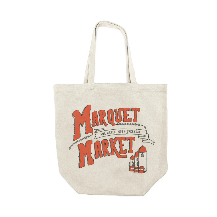 A beige canvas tote bag with large lettering that reads "Marquet Market". In smaller front on a ribbon graphic there are the words "Ank'Harel - Open Everyday". On the bottom right of the tote bag are small orange market stalls and silos.