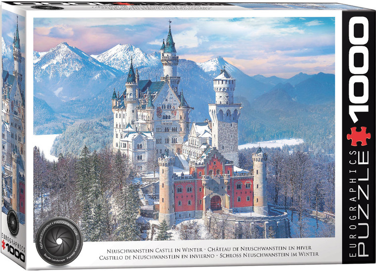 The image displays Neuschwanstein Castle, captured in a winter setting. The castle stands prominently against a backdrop of snow-covered mountains and a slightly cloudy blue sky. The castle, known for its romantic architecture, displays a mix of white and red-toned walls with multiple spires and turrets topped with dark, pointed roofs. It is nestled within a snowy forest landscape. The title, "Neuschwanstein Castle in Winter" is printed along the bottom edge. On the right hand edge, the company logo reads "EUROGRAPHICS PUZZLES" in white text on black background and the number ‘1000’ after it indicates the puzzle piece count. In the bottom left, there is a picture of a camera lens with the words "HDR Photography - Scenic Landscape" printed on the inside rim of the lens. The image displays Neuschwanstein Castle, captured in a winter setting. The castle stands prominently against a backdrop of snow-covered mountains and a slightly cloudy blue sky. The castle, known for its romantic architecture, displays a mix of white and red-toned walls with multiple spires and turrets topped with dark, pointed roofs. It is nestled within a snowy forest landscape. The title, "Neuschwanstein Castle in Winter" is printed along the bottom edge. On the right hand edge, the company logo reads "EUROGRAPHICS PUZZLES" in white text on black background and the number ‘1000’ after it indicates the puzzle piece count. In the bottom left, there is a picture of a camera lens with the words "HDR Photography - Scenic Landscape" printed on the inside rim of the lens.