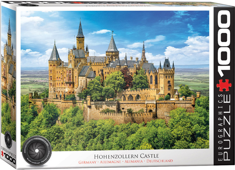 A puzzle titled, “Hohenzollern Castle, Germany,” at the bottom in several different languages.  The company logo “Eurographics Puzzle” is in large font along the right side, and number ‘1000’ right next to it in the cover’s [color] border.  In the center is what the completed puzzle looks like: a brown castle with tall, pointed spires, dark roofing, gothic windows and details, and encircled by dense forest.  It sits atop a mountain, and that forest continues as far as the eye can see.