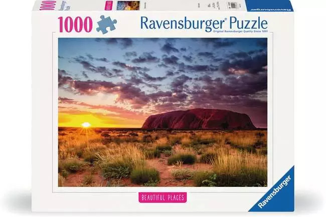 A puzzle with the words “Ravensburger Puzzle” at the top and the number ‘1000’ along the left side of the white bordered cover.  Below is an image of the finished puzzle, which features a photograph of a large, flat, red mountain in the middle of a desert filled with scruffy shrubs and grass.  Above, the sun sets bright orange in the sky.