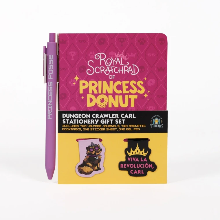 A stationary gift set featuring a small, pink notebook with gold text that reads, "Royal Scratchpad of Princess Donut," with two magnetic book marks in front of it, one which is a long haired tortoise shell cat wearing a crown and one featuring the same crown overtop of pink text that reads, "viva la revolucion, Carl," and a pink pen.