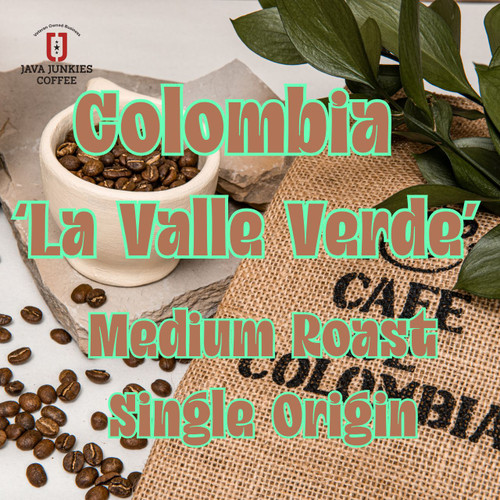 Java Junkies Columbia 'La Valle Verdi' Coffee. White cup of coffee filled with coffee beans sitting next to a burlap bag that says Cafe De Colombia.