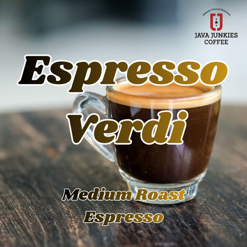 Java Junkies Espresso Verdi Coffee. Clear glass of double espresso sitting on a dark wood table with a white background.
