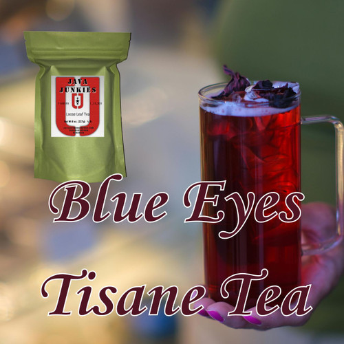 A hand holding a tall glass mug filled with deep red iced Blue Eyes tisane tea garnished with hibiscus petals, accompanied by a green loose leaf tea selection package