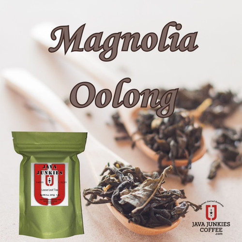 Several small wooden spoons filled with dark, tightly rolled loose-leaf magnolia oolong tea rest neatly on a soft, light-toned surface.