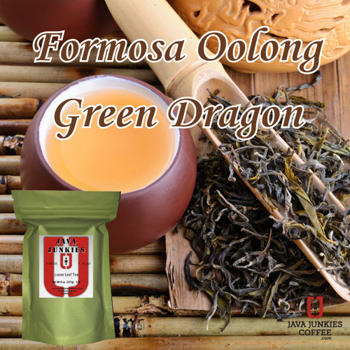 A small brown ceramic teacup filled with warm amber-hued tea, accompanied by loose oolong leaves on a bamboo mat next to a wooden scoop
