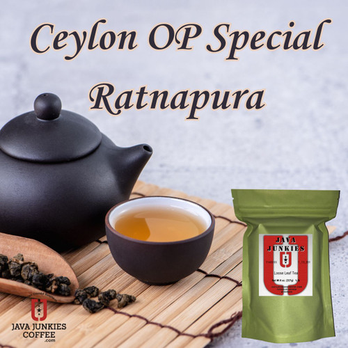 A dark clay teapot, a matching teacup filled with amber tea, and a wooden scoop of loose leaves resting on a bamboo mat.