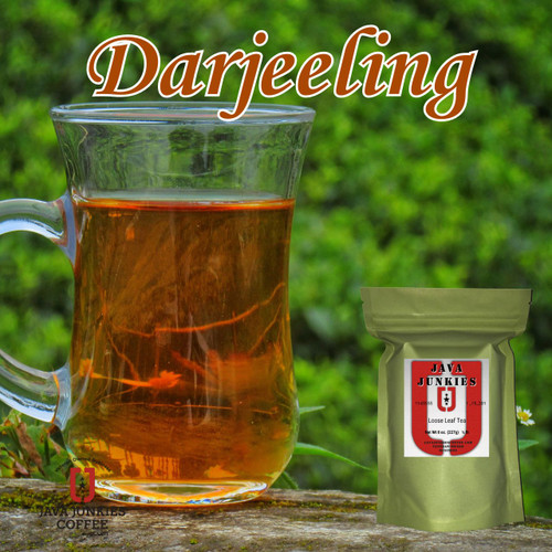 A clear glass mug filled with amber Darjeeling tea resting on a mossy wooden surface alongside a green product pouch.