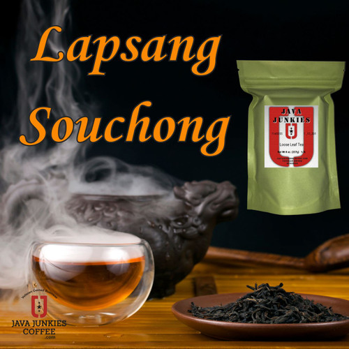A double-walled glass cup filled with amber tea surrounded by rising smoke, a dark teapot, and a small dish of loose black tea leaves on a wooden table.