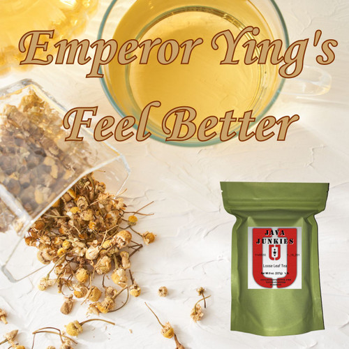 A glass mug of golden chamomile tea next to a glass container spilling dried chamomile flowers across a white surface, accompanied by a green loose leaf tea selection.