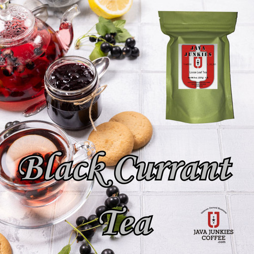 A clear teacup filled with red berry tea and lemon slices sits next to a glass jar of dark fruit preserves, fresh black currants, and cookies on a white tile surface.