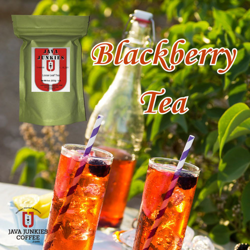 Two tall glasses filled with iced blackberry tea, garnished with fresh blackberries and purple striped straws, set outdoors against a backdrop of green foliage and a glass bottle.
