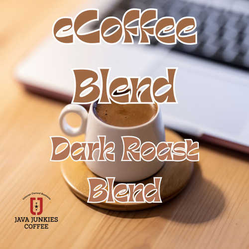 Java Junkies eCoffee Blend Coffee. White modern coffee mug filled with creamy coffee on a wood coaster next to a laptop.