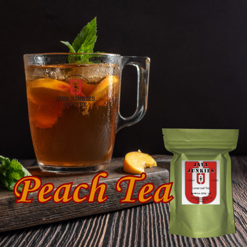 A large glass mug filled with iced peach tea garnished with fresh peach slices and mint leaves, sitting on a wooden board next to a green tea pouch.